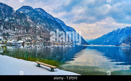 Die Sitzbank auf der Bank von snowy Badeinsel Naherholungsgebiet von Hallstatt mit Blick auf klare Hallstattersee See Oberfläche, Salzberg und Altstadt Stockfoto