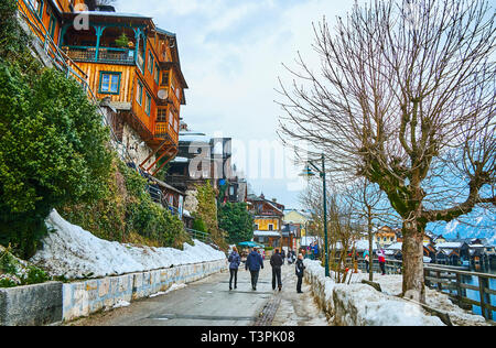 HALLSTATT, Österreich - 21. FEBRUAR 2019: Spaziergang die ruhigen Winter Seepromenade - Seestraße mit Schneeverwehungen auf den Seiten und bunten Holzhäusern Stockfoto