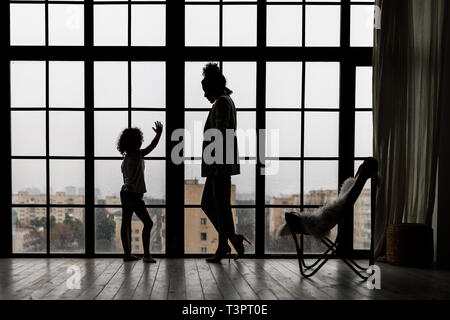 Seitenansicht der liebevollen Mutter und Tochter umarmt von Fenster Stockfoto