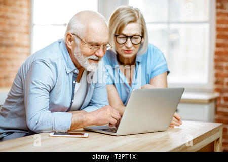 Porträt einer wunderschönen senior Paar in blauen Shirts Gefühl glücklich zusammen sitzen mit Laptop zu Hause Stockfoto
