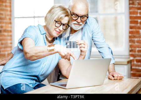 Gerne älteres Paar Einkaufen online mit Kreditkarte und Laptop zu Hause Stockfoto