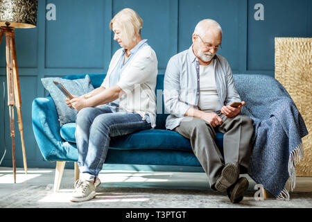Älterer Mann und Frau zurück zu jedem anderen sitzt beleidigt, mit digitalen Gadgets auf der Couch zu Hause Stockfoto