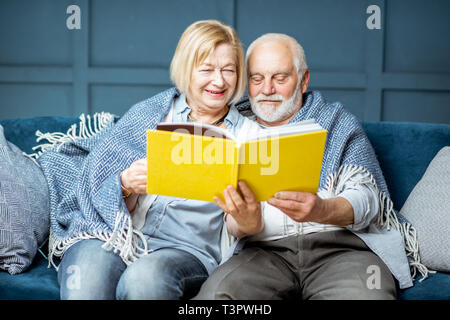 Schönes älteres Paar lesen Buch sitzend mit warmem Plaid auf der Couch zu Hause gewickelt Stockfoto