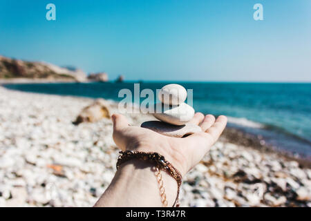 Gleichgewicht der Steine auf der Hand vor dem Hintergrund des Meeres. Der Begriff der Ruhe, Harmonie, Spiritualität Stockfoto