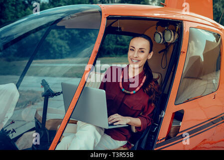 Langhaarige attraktive Frau mit breiten Grinsen mit Laptop Stockfoto