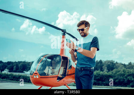 Lächelnd gut aussehender Mann in Sonnenbrille Kontrolle soziale Medien Stockfoto