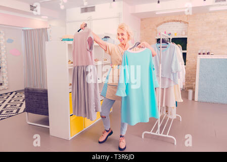 Stilvolle Frau mittleren Alters entscheiden, welches Kleid zu kaufen Stockfoto