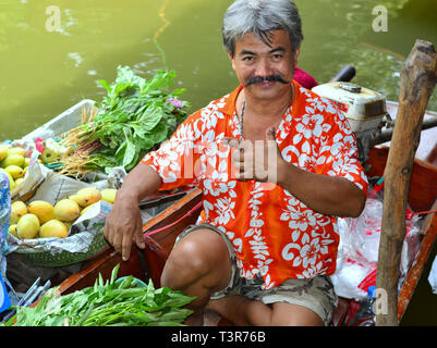 Fröhlichen Thai boot Anbieter verkauft frisches grünes Gemüse und süßen Mangos von seinem Boot und posiert für die Kamera. Stockfoto