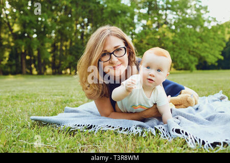 Mutter mit Kind spielen auf Gras bei Sonnenuntergang im Sommer Stockfoto