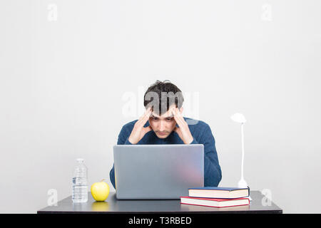 Frustriert und männlicher Student an einem Laptop suchen betont. Müde im Büro am Schreibtisch mit Computer und Überstunden Projekt sitzen. Überlastung Stockfoto