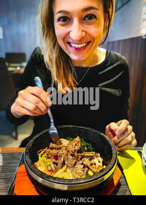 Koreanische bibimbap diente in Hot Stone dolsot Topf Schüssel von kaukasischen lächelnde Frau Speisen in der koreanischen ethnischen Restaurant gegessen Stockfoto