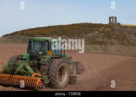 Ein Landwirt Eggen ein Feld unter dem War Memorial in der Nähe von Stonehaven in Aberdeenshire Stockfoto