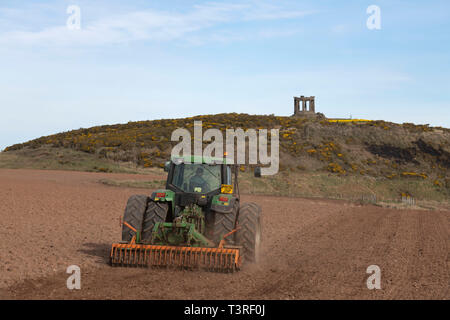 Ein Landwirt Eggen ein Feld unter dem War Memorial in der Nähe von Stonehaven in Aberdeenshire Stockfoto