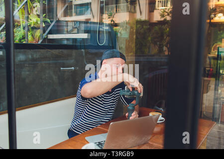 Der Mann mit dem Telefon auf dem Stabilisator führt die Vlog. Er nimmt sich selbst in die Kamera. Ändern Sie die Einstellungen, indem Sie auf den Auslöser. Smartphone Stockfoto