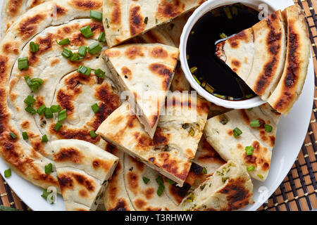 Frisch gebratene Chinesische grüne Zwiebel Pfannkuchen auf einer Servierplatte mit Sojasoße horizontale Ansicht von oben, close-up. Makro, flatlay Stockfoto