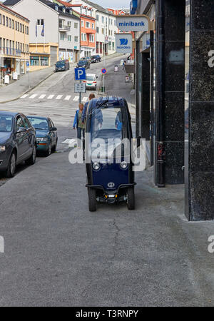 Eine Blaue abgedeckt Norwegische Mobilität scooter außerhalb einer Bank auf dem Gehsteig von einem steilen Hügel auf einem Sommertag in Kristiansund, Norwegen geparkt. Stockfoto