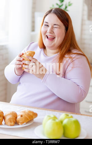 Happy positive chubby Frau essen ein Croissant Stockfoto