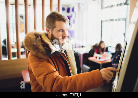 Ein Mann Bestellungen Essen im Touch Screen Terminal mit elektronischen Menü in Fast Food Restaurant. Stockfoto