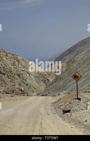 Schmutz der Straße bergab durch felsige öde Landschaft führenden Küste in der Atacama-wüste zu Pacific, Chile Stockfoto