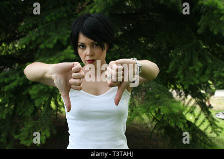 Schöne dunkelhaarige Dame mit einem weißen Top, Handzeichen. Zwei Daumen nach unten. Stockfoto