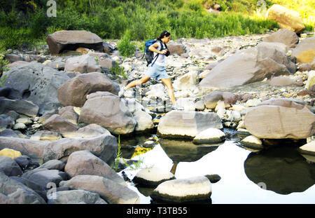 Kaukasische Frau springen auf Felsen im Fluss Stockfoto