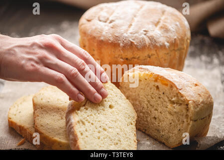 Frauen Hände brechen hausgemachten Naturprodukten frisches Brot mit einer goldenen Kruste auf eine Serviette auf einem alten Holz- Hintergrund. Das Konzept der Backen Backwaren Stockfoto