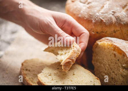 Frauen Hände brechen hausgemachten Naturprodukten frisches Brot mit einer goldenen Kruste auf eine Serviette auf einem alten Holz- Hintergrund. Konzept der Backen Backwaren Stockfoto