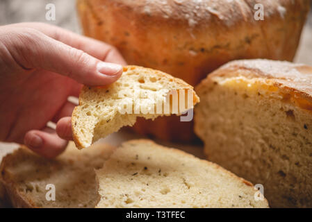 Frauen Hände brechen hausgemachten Naturprodukten frisches Brot mit einer goldenen Kruste auf eine Serviette auf einem alten Holz- Hintergrund. Konzept der Backen Backwaren Stockfoto