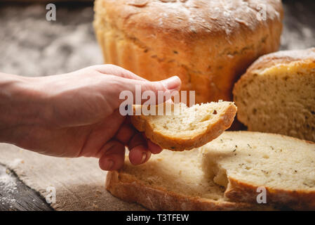 Frauen Hände brechen hausgemachten Naturprodukten frisches Brot mit einer goldenen Kruste auf eine Serviette auf einem alten Holz- Hintergrund. Konzept der Backen Backwaren Stockfoto