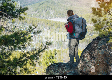 Man touristische Wanderer mit einem großen Rucksack steht auf einer Felswand und schaut auf die Weiten grünen Tal. Der Begriff der Freiheit in der Reise Stockfoto