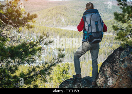 Man touristische Wanderer mit einem großen Rucksack steht auf einer Felswand und schaut auf die Weiten grünen Tal. Der Begriff der Freiheit in der Reise Stockfoto