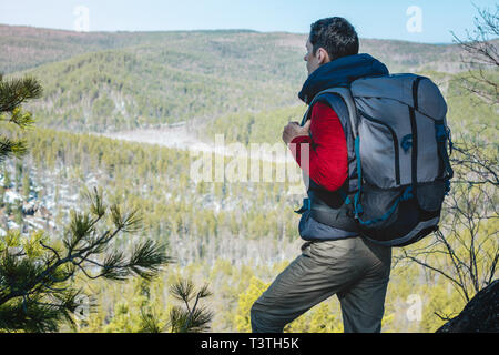 Man touristische Wanderer mit einem großen Rucksack steht auf einer Felswand und schaut auf die Weiten grünen Tal. Der Begriff der Freiheit in der Reise Stockfoto