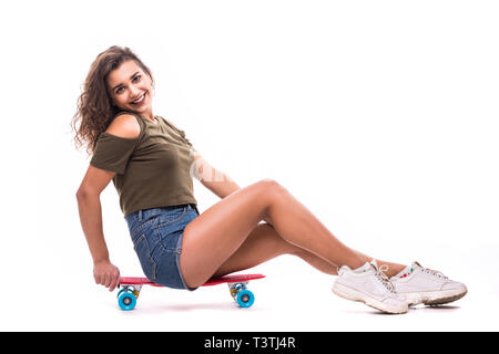 Lächelnde hübsche Frau sitzt auf dem Skateboard isoliert auf weißem Hintergrund Stockfoto