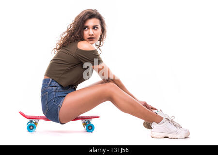 Lächelnde hübsche Frau sitzt auf dem Skateboard isoliert auf weißem Hintergrund Stockfoto