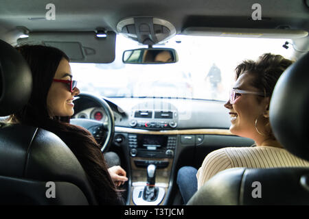 Lächelnd glückliche junge Frau, die ihrem Freund einen Aufzug in Ihrem Auto in der Stadt, durch das offene Seitenfenster mit Sun flare Stockfoto
