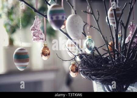 Zweige mit Knospen in einem Nest fest. Sie sind mit österlichen Motiven verziert. Handbemalte Ostereier und glänzend Osterhasen. Tischdekoration in Fron Stockfoto