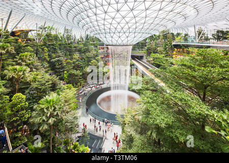Heller und geräumiger Blick auf den Indoor-Wasserfall am Jewel Changi Airport tagsüber, Singapur. Die Räume sind mit üppigen, gruseligen Bäumen gefüllt. Stockfoto
