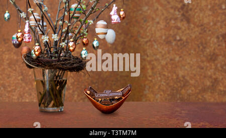 Branchen mit Blüten und Knospen. Ostereier und Osterhasen hängen an den Zweigen und Schwingen. Schüssel aus Kupfer mit Schokolade gefärbt. Stockfoto