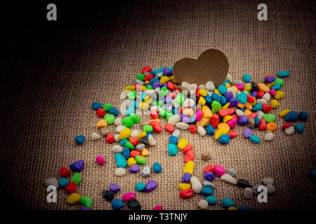 Herz aus Papier inmitten der bunten Steinchen auf Leinwand Boden Stockfoto