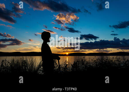 Sillhouette von einem Jungen auf einem Roller bei Sonnenuntergang mit Blick über den Hudson River, Tarrytown, New York, NY Stockfoto