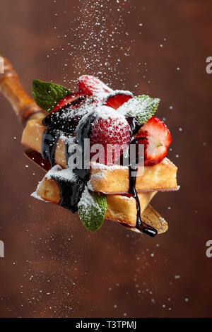 Belgische Waffeln mit Erdbeeren, Minze und Schokoladensauce, bestreut mit Puderzucker. Stockfoto