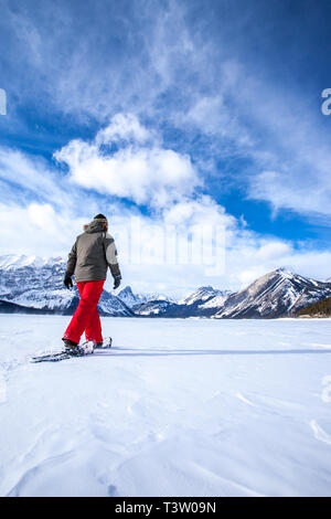 Junge Frau Schneeschuhwandern auf einem zugefrorenen See in den kanadischen Rocky Mountains, Kananaskis, Alberta, Kanada Stockfoto