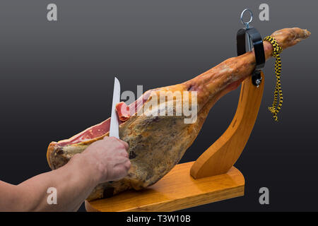 Hand schneidet mit dem Messer an einer spanischen Serrano Schinken in einem Holz-Halter - isoliert Stockfoto