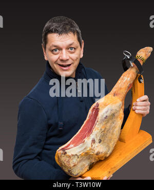 Mann hält ein spanischer Serrano Schinken auf den Oberschenkel mit Holz Halter Stockfoto