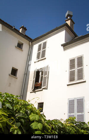 Schöne weiße 3-stöckiges Gebäude mit schlechter Fensterläden auf dem Hintergrund einer Zaun bedeckt mit grünem Efeu, Paris, Frankreich. Stockfoto