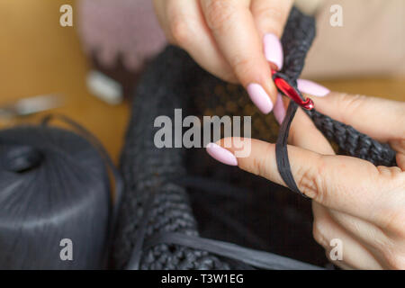 Hands of a young woman knit hat from black synthetic yarn on a light wooden surface. Selective soft focus. Stockfoto