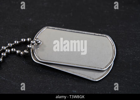 Nahaufnahme der blank military Dog Tags mit Kette auf schwarzem Schiefer Stockfoto