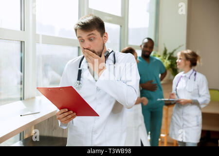 Schön überrascht der männlichen professionellen Arzt stehen über Krankenhaus Hintergrund. Werbung Bild über das Gesundheitswesen, Gesundheit, Klinik, Medizin. Stockfoto