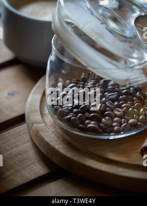 Glas ist teilweise mit natürlichen Kaffeebohnen gefüllt. In der Nähe befindet sich eine süße Erdbeere Cupcake. Stockfoto