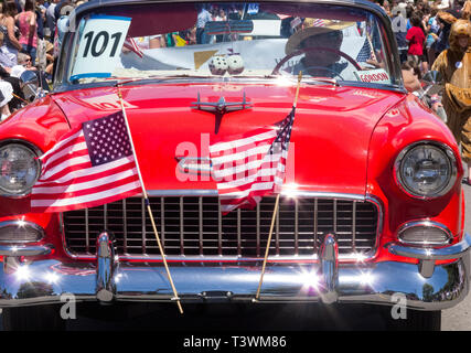 Mann, der ein klassisches Chevrolet Bel Air Auto Automobil mit amerikanischen Fahnen in einem traditionellen kleinen Stadt Viertel der Juli Parade eingerichtet Stockfoto